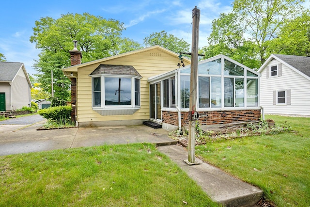 5540 Cozy Point Dr, Newaygo, MI 49337 - view of front of house with brick siding, a chimney, a front yard, a sunroom, and a patio