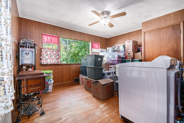 clothes washing area with washer / clothes dryer, light hardwood / wood-style flooring, wooden walls, ornamental molding, and ceiling fan