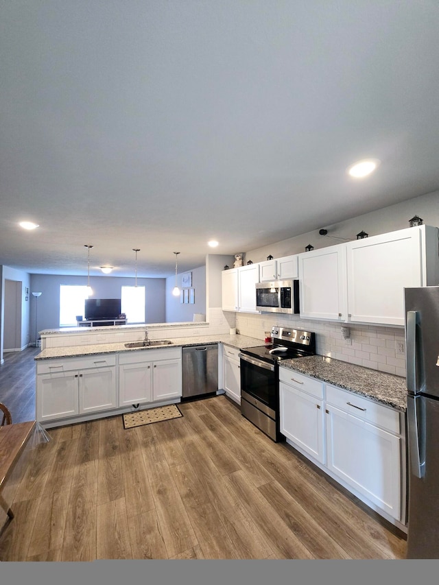 kitchen featuring light hardwood / wood-style flooring, appliances with stainless steel finishes, hanging light fixtures, kitchen peninsula, and white cabinetry