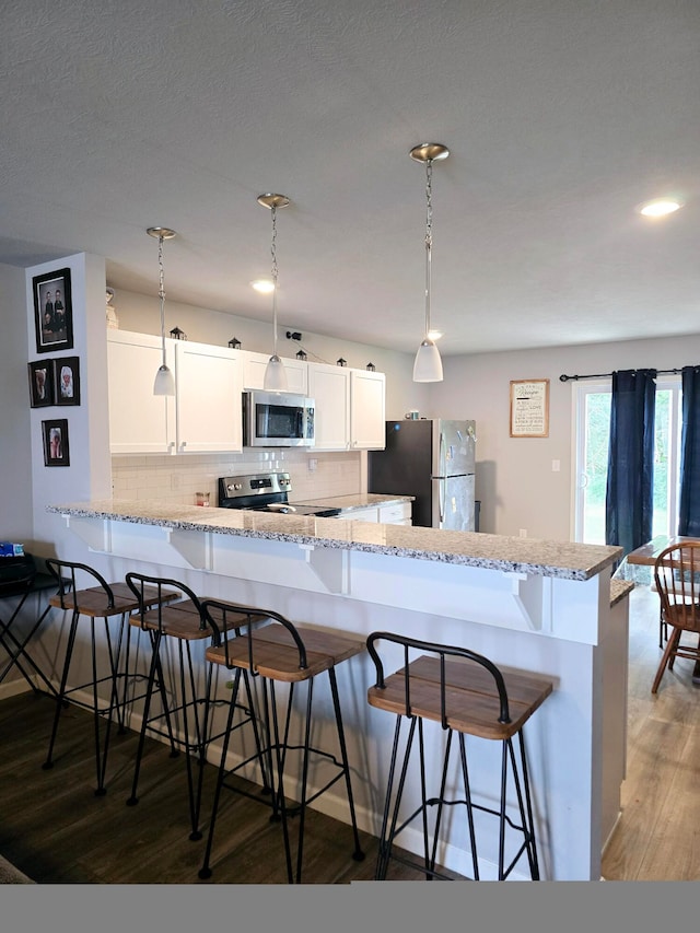 kitchen featuring white cabinets, decorative light fixtures, appliances with stainless steel finishes, dark hardwood / wood-style flooring, and a kitchen bar