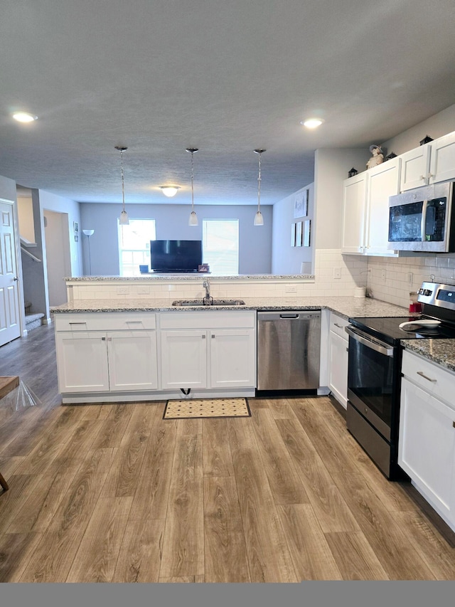 kitchen with pendant lighting, light hardwood / wood-style flooring, stainless steel appliances, and kitchen peninsula