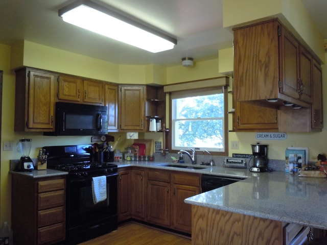 kitchen featuring light wood-type flooring, black appliances, kitchen peninsula, and sink