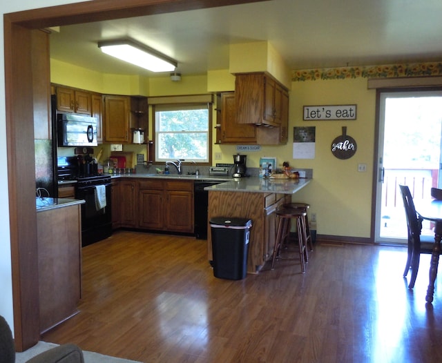 kitchen with dark wood-type flooring, black appliances, kitchen peninsula, and sink