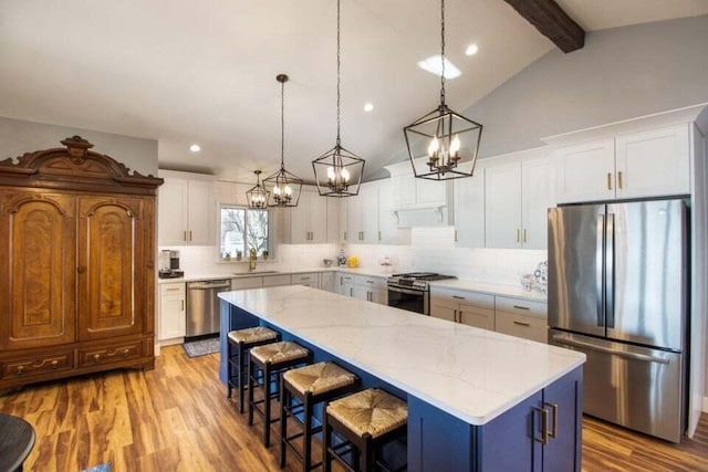 kitchen featuring white cabinets, a center island, lofted ceiling with beams, appliances with stainless steel finishes, and wood-type flooring