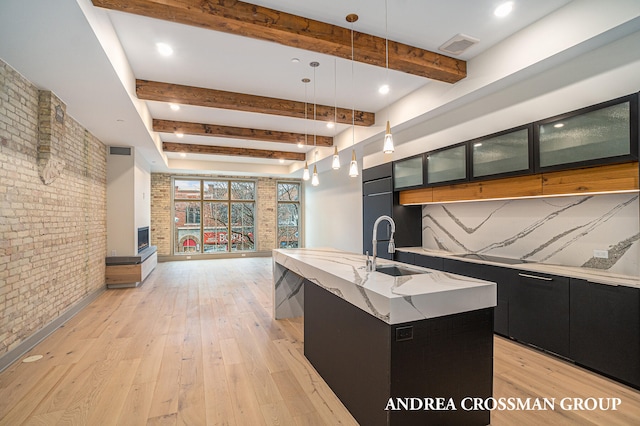 kitchen with a large island with sink, brick wall, beam ceiling, and decorative light fixtures