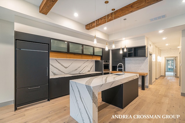 kitchen featuring decorative backsplash, stainless steel oven, a spacious island, light wood-type flooring, and pendant lighting