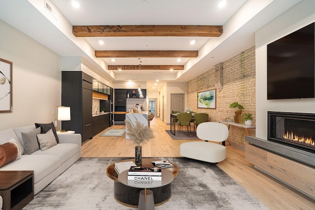 living room featuring a large fireplace, brick wall, beam ceiling, and light hardwood / wood-style floors