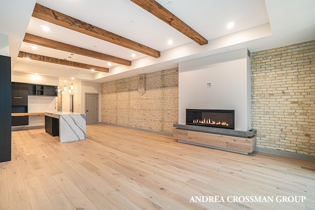 unfurnished living room featuring beam ceiling, brick wall, and light wood-type flooring