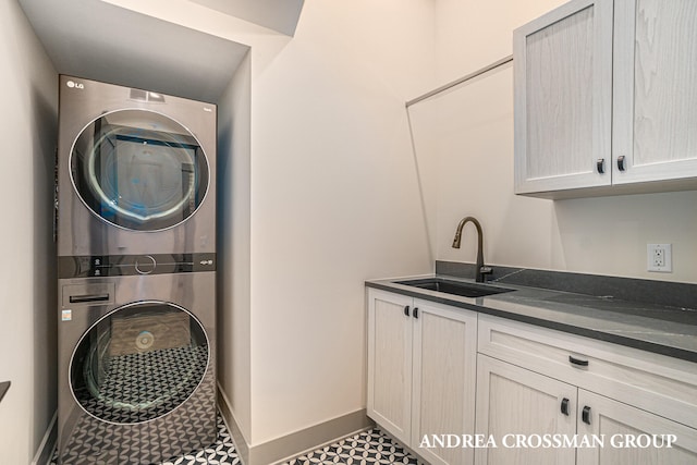 clothes washing area with stacked washing maching and dryer, cabinets, and sink