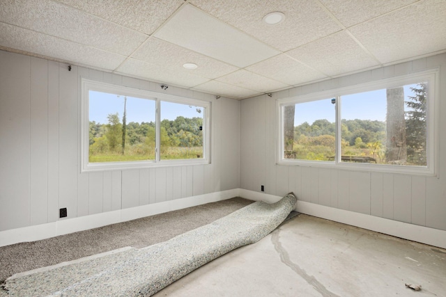 unfurnished room featuring plenty of natural light, a paneled ceiling, and wooden walls