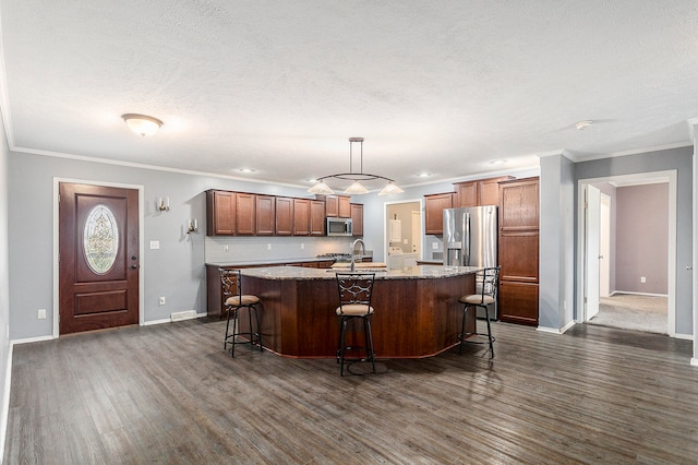 kitchen with dark hardwood / wood-style floors, pendant lighting, an island with sink, a kitchen bar, and stainless steel appliances