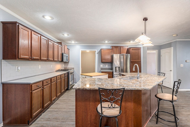 kitchen with a kitchen breakfast bar, stainless steel appliances, an island with sink, and light hardwood / wood-style flooring