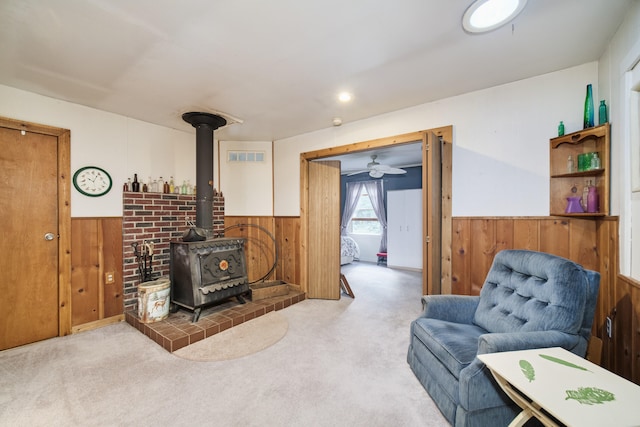 living room with ceiling fan, light colored carpet, a wood stove, and wood walls