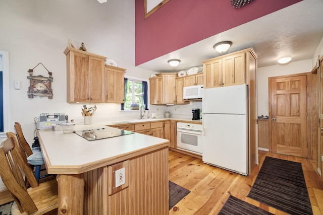 kitchen with a breakfast bar area, light brown cabinetry, kitchen peninsula, and white appliances