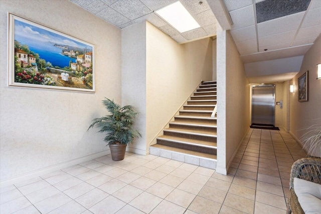 stairs with a paneled ceiling, elevator, and tile patterned floors