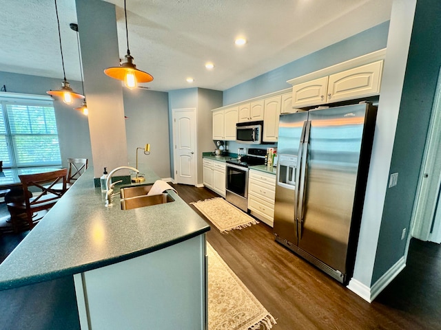 kitchen featuring dark hardwood / wood-style floors, pendant lighting, appliances with stainless steel finishes, sink, and white cabinetry