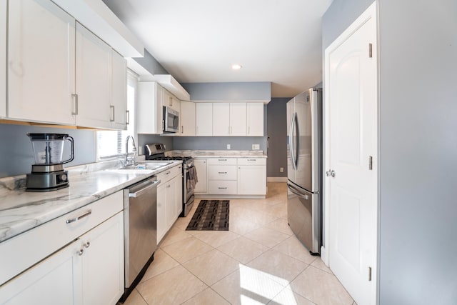 kitchen featuring white cabinets, light tile patterned floors, appliances with stainless steel finishes, light stone countertops, and sink