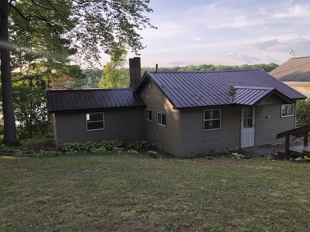 rear view of house featuring a lawn, a chimney, and metal roof