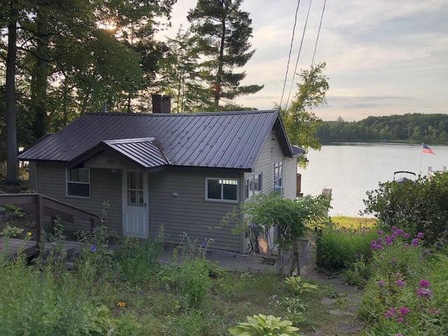 exterior space with metal roof, a water view, and a chimney