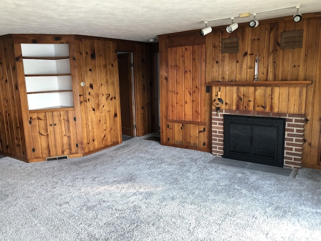 unfurnished living room with a textured ceiling, wooden walls, a brick fireplace, and carpet floors