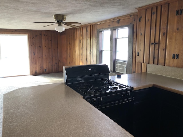 kitchen featuring cooling unit, black range with gas cooktop, wood walls, ceiling fan, and a textured ceiling