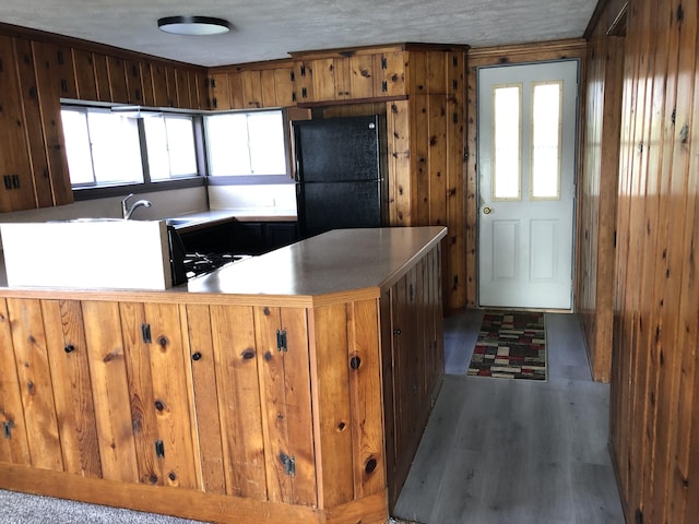 kitchen featuring a textured ceiling, black refrigerator, wood walls, kitchen peninsula, and dark wood-type flooring