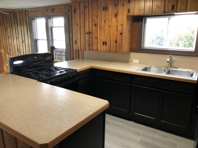 kitchen featuring light hardwood / wood-style flooring, wood walls, sink, and gas stove