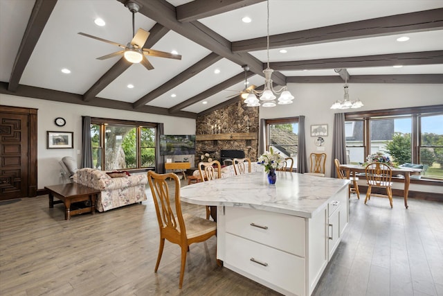 interior space featuring ceiling fan with notable chandelier, a wealth of natural light, white cabinets, and a stone fireplace