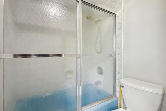 bathroom featuring toilet and combined bath / shower with glass door