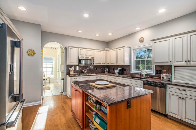 kitchen with dark stone counters, light hardwood / wood-style flooring, sink, a center island, and appliances with stainless steel finishes