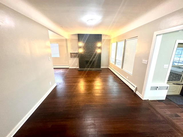 unfurnished living room with dark wood-type flooring, a baseboard heating unit, and a healthy amount of sunlight