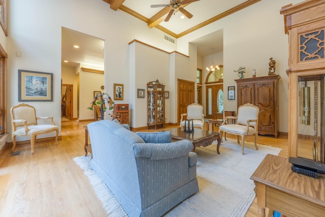 living room featuring ceiling fan with notable chandelier, light wood-type flooring, ornamental molding, and a towering ceiling