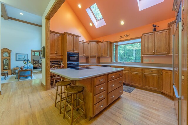 kitchen with a breakfast bar area, light hardwood / wood-style flooring, a center island, high vaulted ceiling, and a skylight