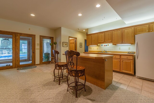 kitchen featuring a kitchen breakfast bar, white fridge, light tile patterned floors, a center island, and sink