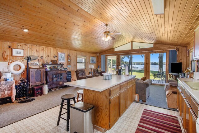 kitchen with lofted ceiling, kitchen peninsula, wood walls, ceiling fan, and a breakfast bar