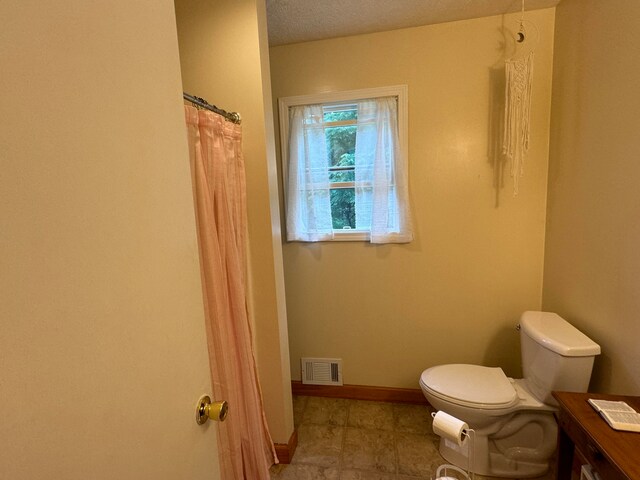 bathroom featuring a shower with curtain, toilet, and a textured ceiling