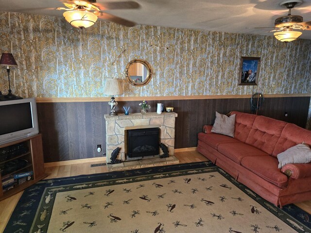 living room with ceiling fan, wood-type flooring, and a stone fireplace