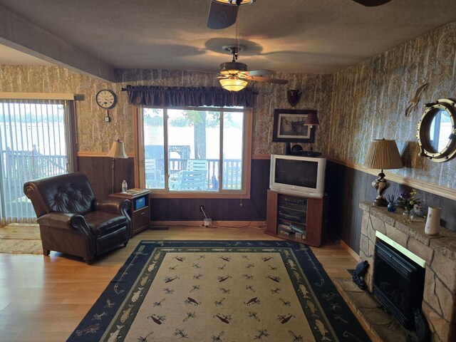 living room with plenty of natural light, ceiling fan, a stone fireplace, and wood-type flooring