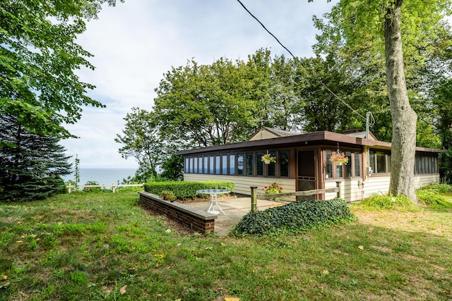 back of property with a water view, a lawn, and a sunroom