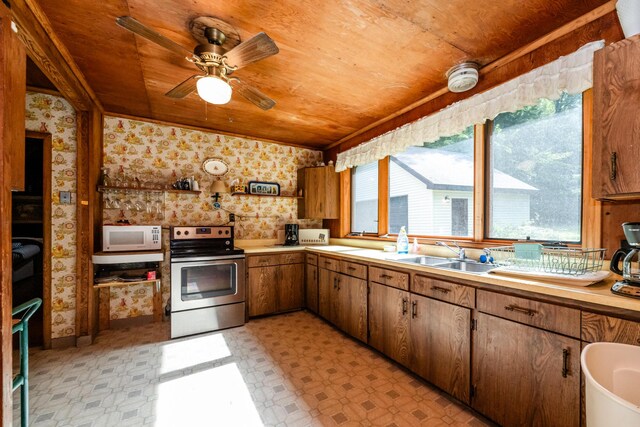 kitchen featuring white microwave, wallpapered walls, stainless steel electric range, plenty of natural light, and a sink