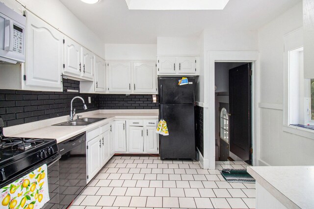 kitchen featuring tasteful backsplash, white cabinetry, black appliances, a skylight, and sink