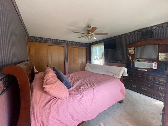 bedroom with carpet flooring, ceiling fan, and two closets