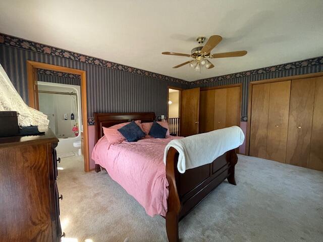 bedroom with ensuite bathroom, ceiling fan, carpet floors, and multiple closets