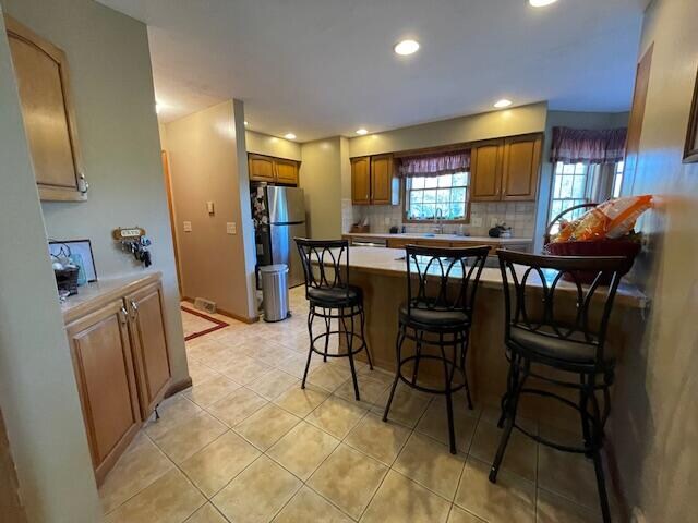 kitchen with stainless steel fridge, light tile patterned floors, decorative backsplash, and a breakfast bar