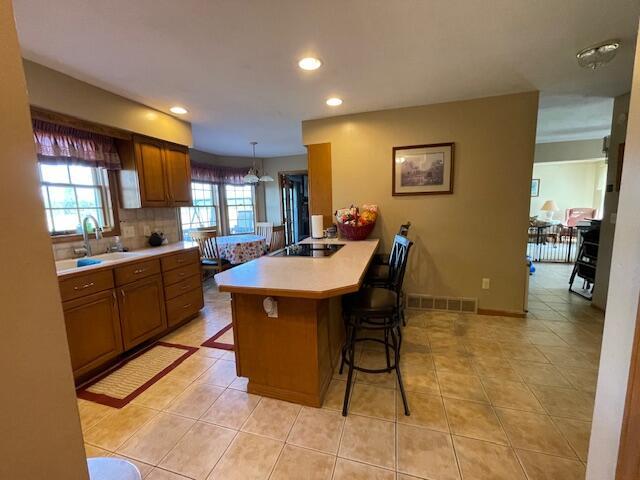 kitchen featuring a breakfast bar area, decorative light fixtures, tasteful backsplash, kitchen peninsula, and black electric cooktop