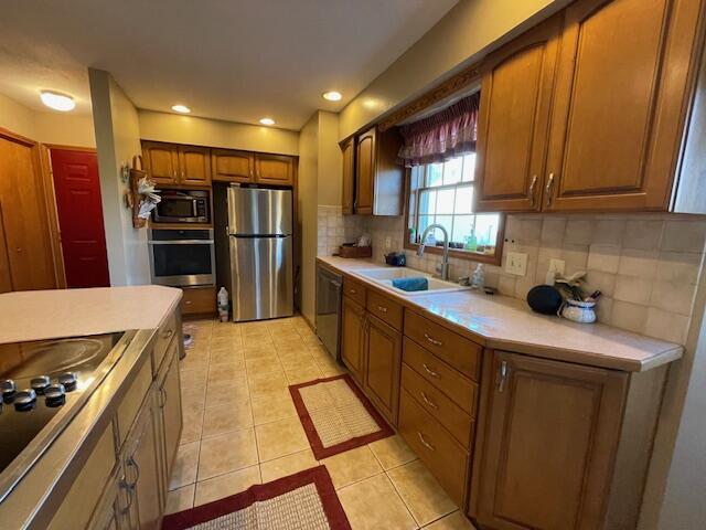 kitchen featuring appliances with stainless steel finishes, light tile patterned floors, backsplash, and sink