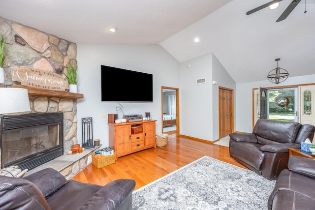 living room with lofted ceiling, light hardwood / wood-style flooring, ceiling fan, and a stone fireplace