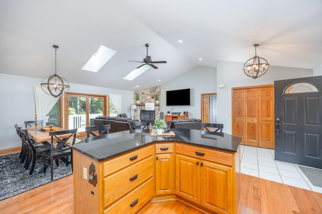 kitchen featuring light wood-type flooring, lofted ceiling with skylight, ceiling fan with notable chandelier, decorative light fixtures, and a center island