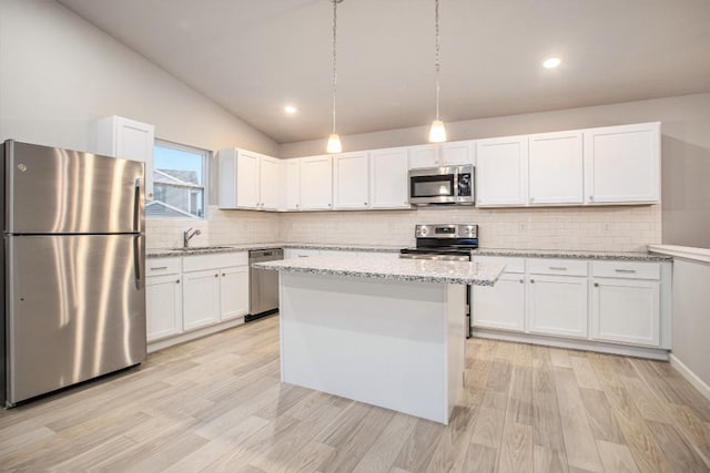 kitchen with appliances with stainless steel finishes, white cabinets, a kitchen island, light stone countertops, and lofted ceiling