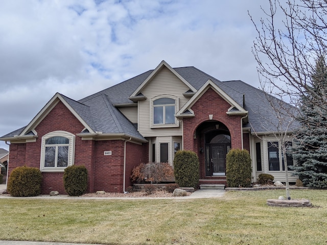 view of front facade with a front lawn, brick siding, and roof with shingles